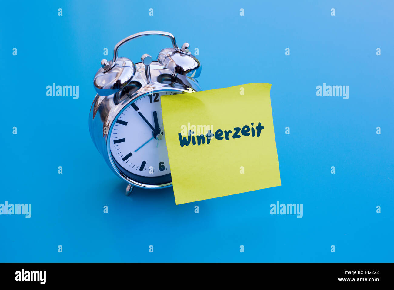 alarm clock on blue table with sticky note with german word 'Winterzeit' (winter time) Stock Photo