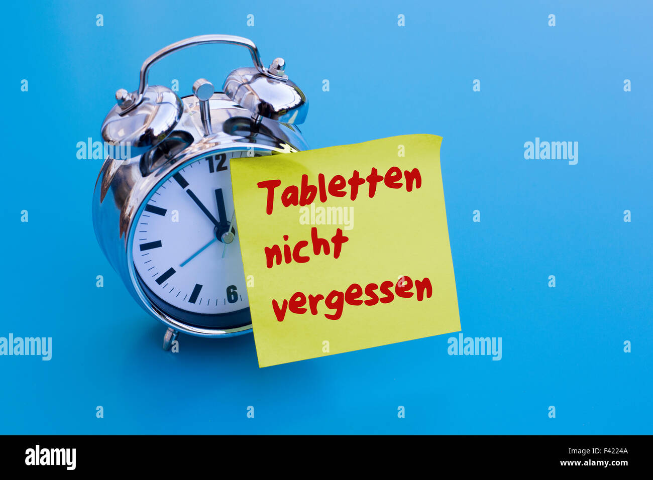 alarm clock on blue table with sticky note with german words 'Tabletten nicht vergessen' (don't forget your pills) Stock Photo