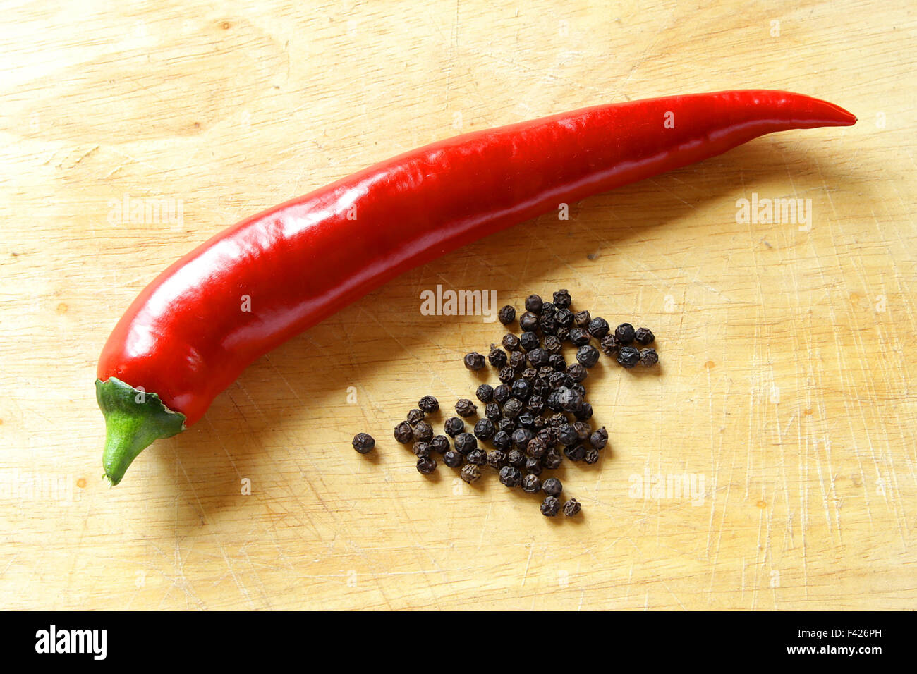 long red hot pepper shiny on kitchen board with dried black peppers Stock Photo