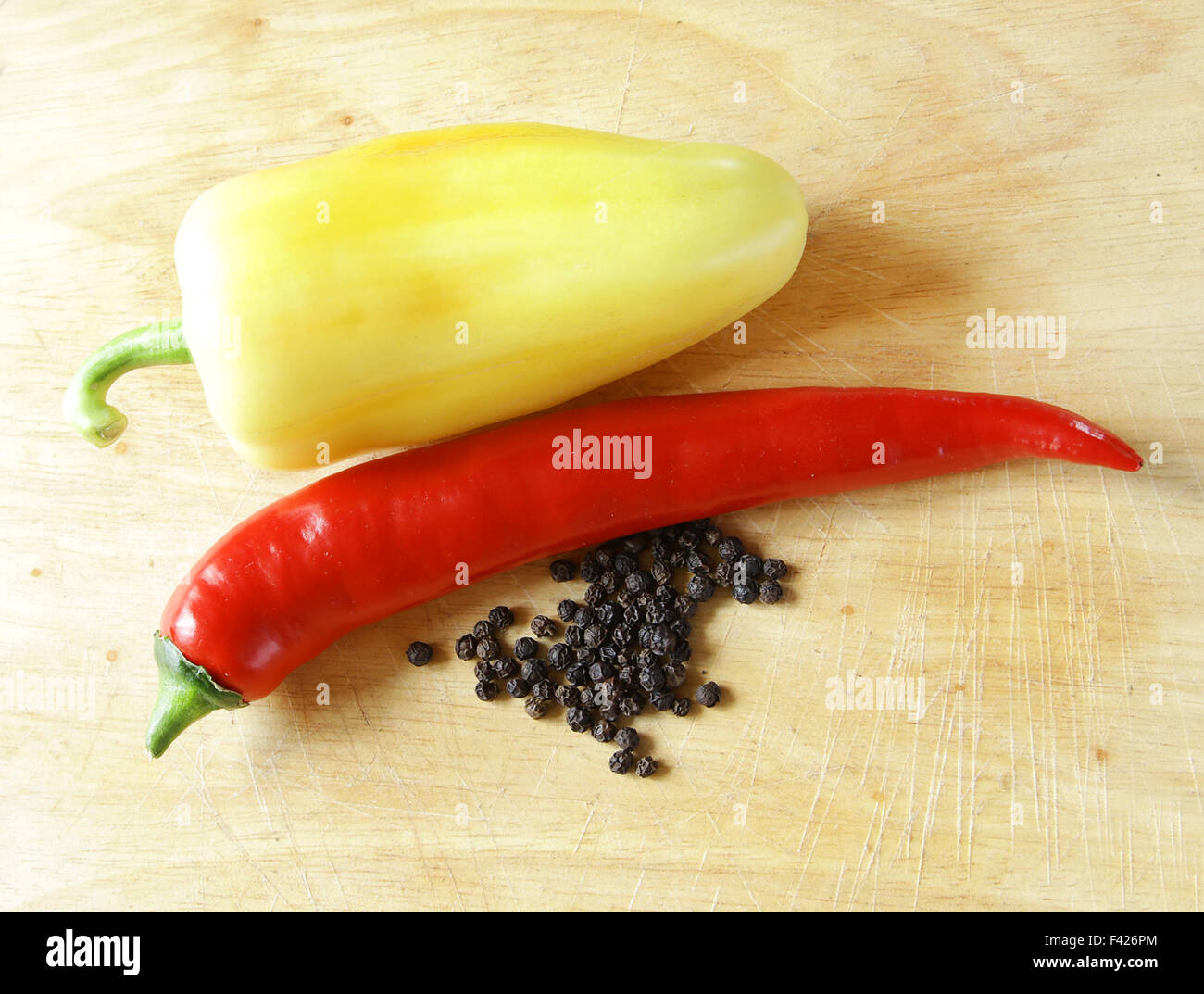 long red hot pepper shiny on kitchen board with dried black peppers and paprika Stock Photo