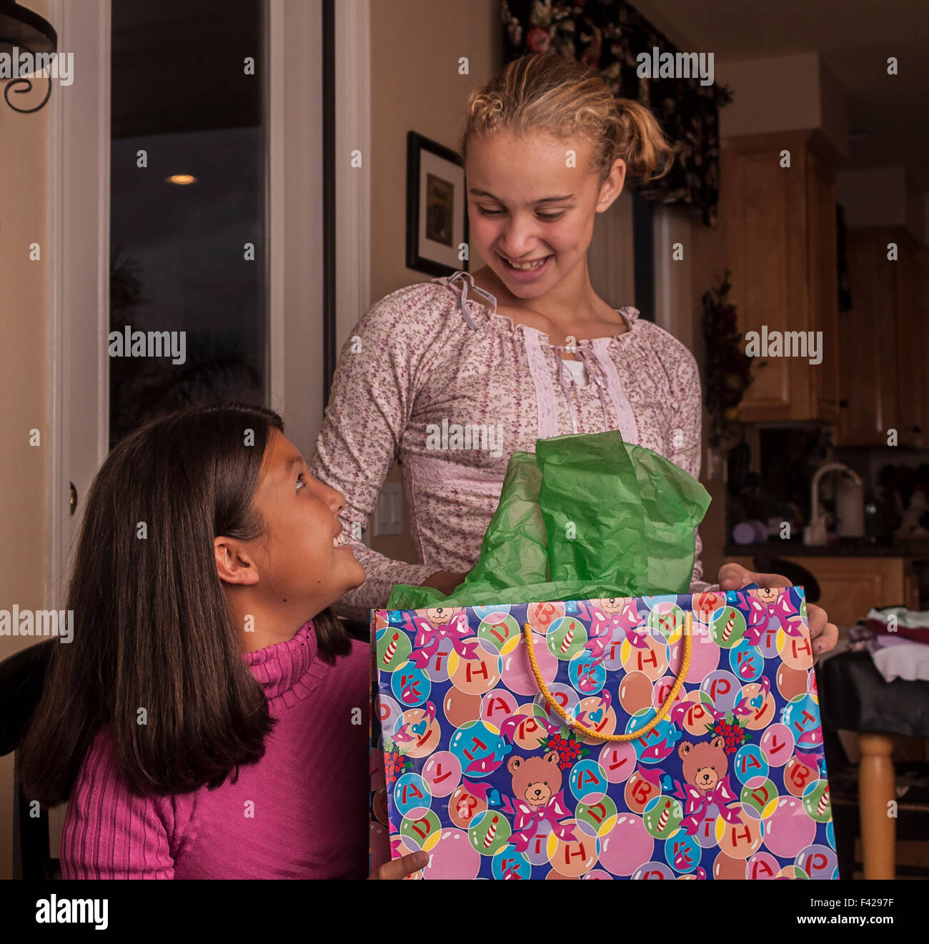 Child giving gift to child interracial multicultural multi ethnic Korean and Brazilian best girl friends opening presents gifts. MR ©Myrleen Pearson Stock Photo