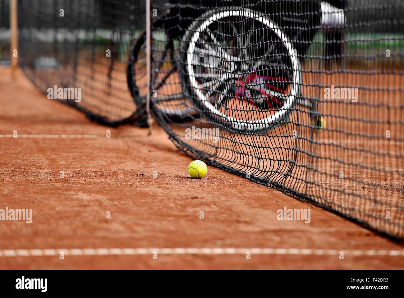 Unfocused wheelchair tennis player is seen behind a tennis net on a clay court Stock Photo