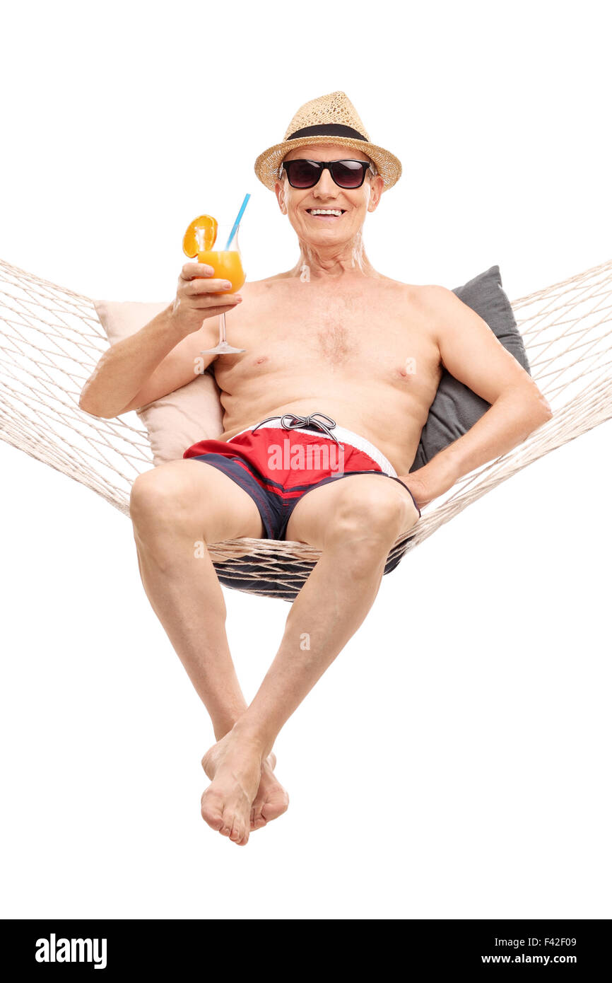 Joyful senior in red swim trunks lying in a hammock and drinking an orange cocktail isolated on white background Stock Photo