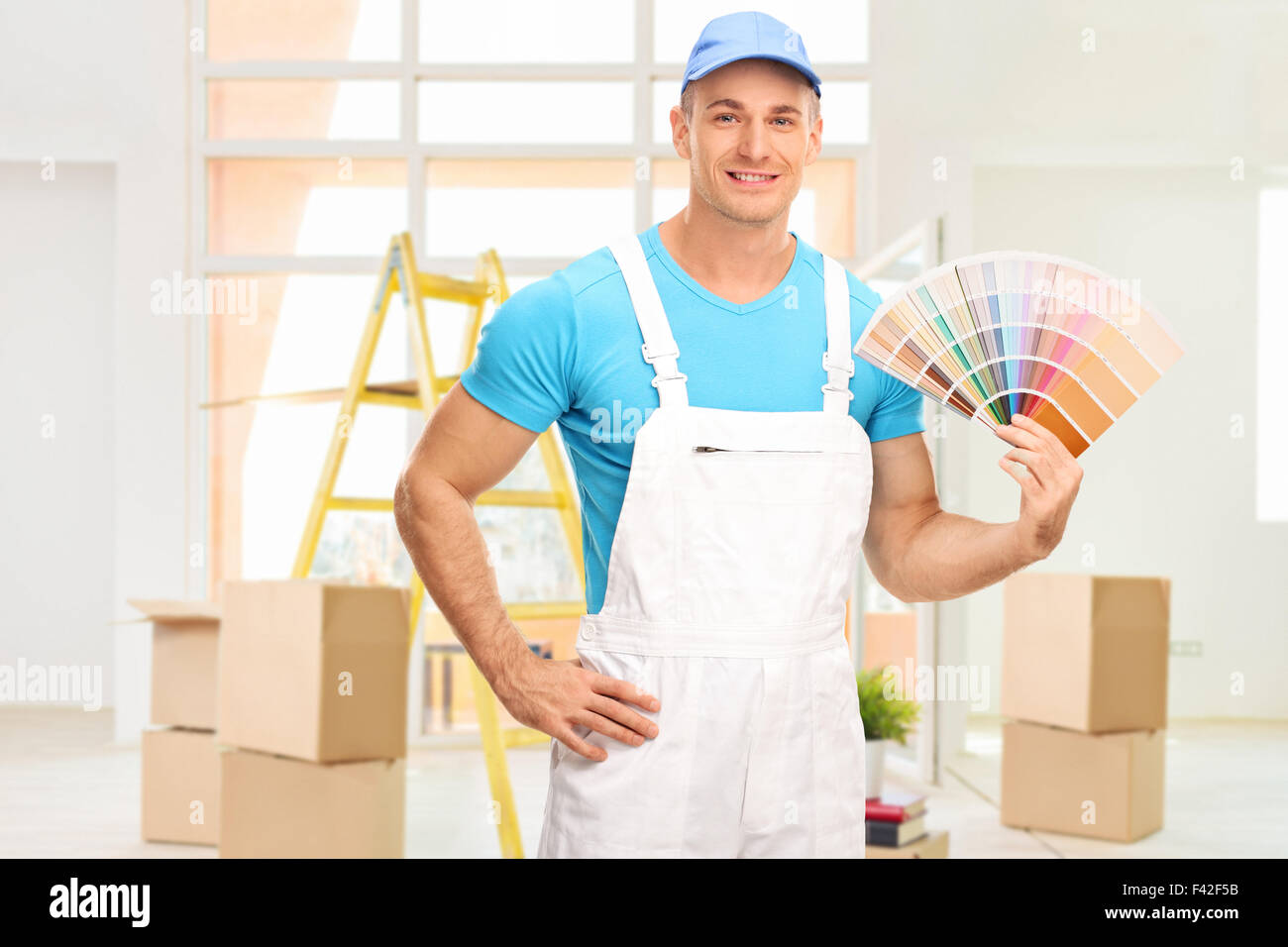 Young male house painter in a white jumpsuit holding a color swatch in an apartment and looking at the camera Stock Photo
