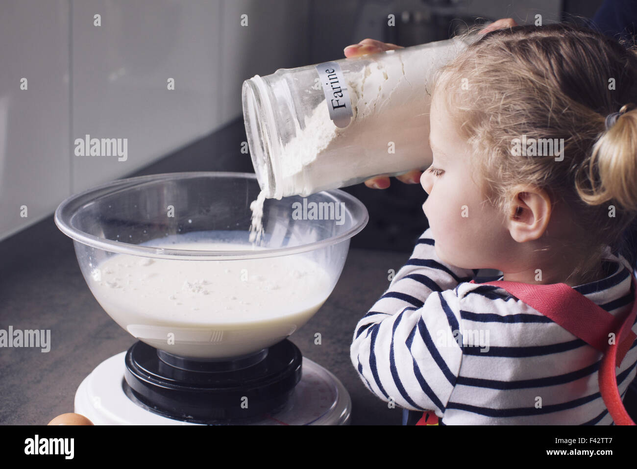 Little girl pouring flour into mixing bowl Stock Photo