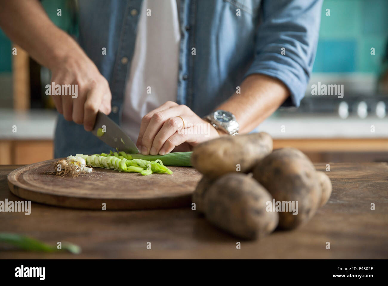 Man cutting spring onion in kitchen Stock Photo