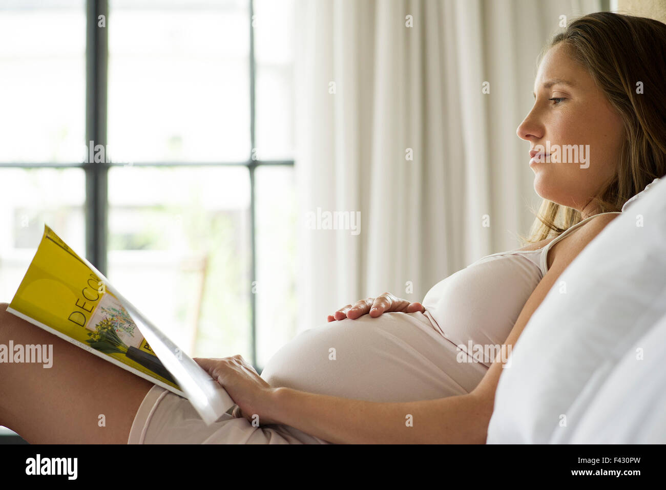 Pregnant woman reading magazine in bed Stock Photo