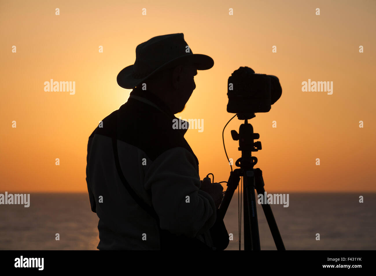 Photographer silhouetted in sunset taking photos at Chesil Beach, Portland, Weymouth, Dorset UK in October Stock Photo