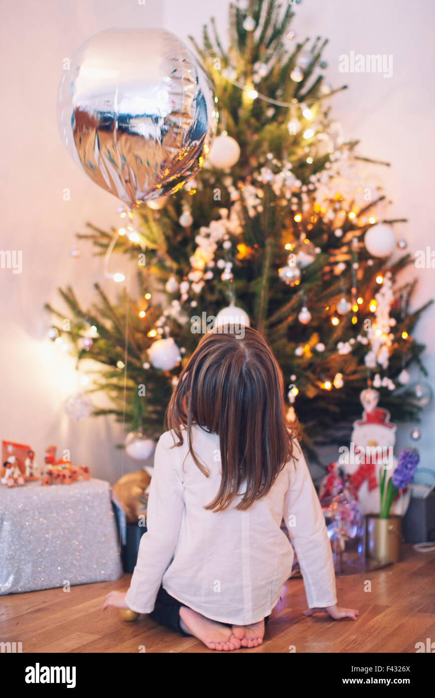 Girl sitting on floor gazing up at Christmas tree Stock Photo