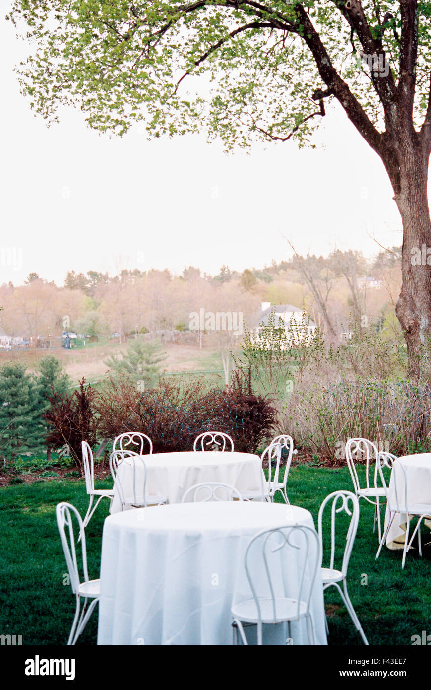 Tables and chairs set with white table clothes in a hotel garden overlooking a wooded valley. Stock Photo