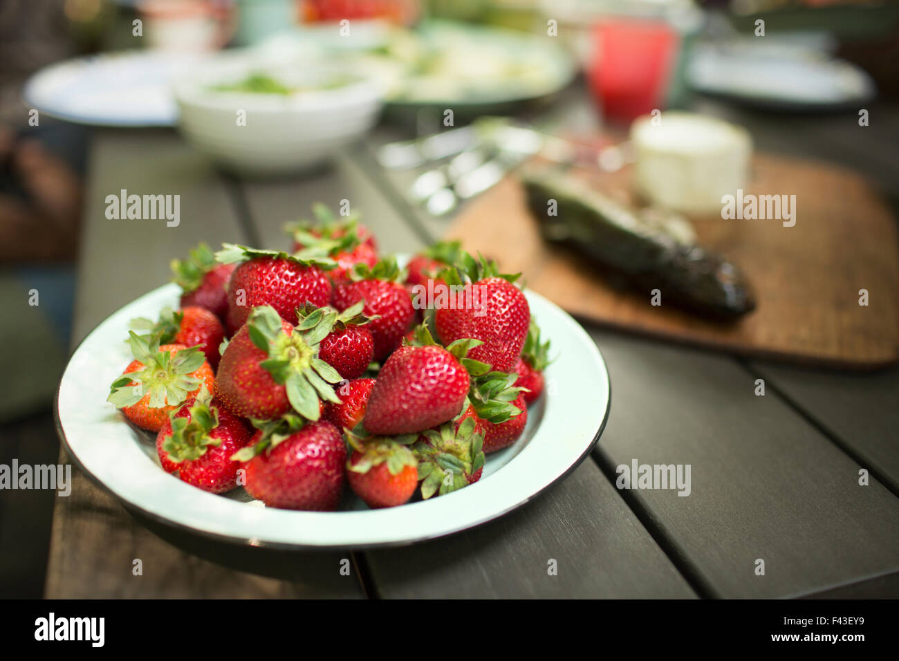 Picnic table with a meal laid out. A place of fresh home grown newly picked strawberries. Stock Photo