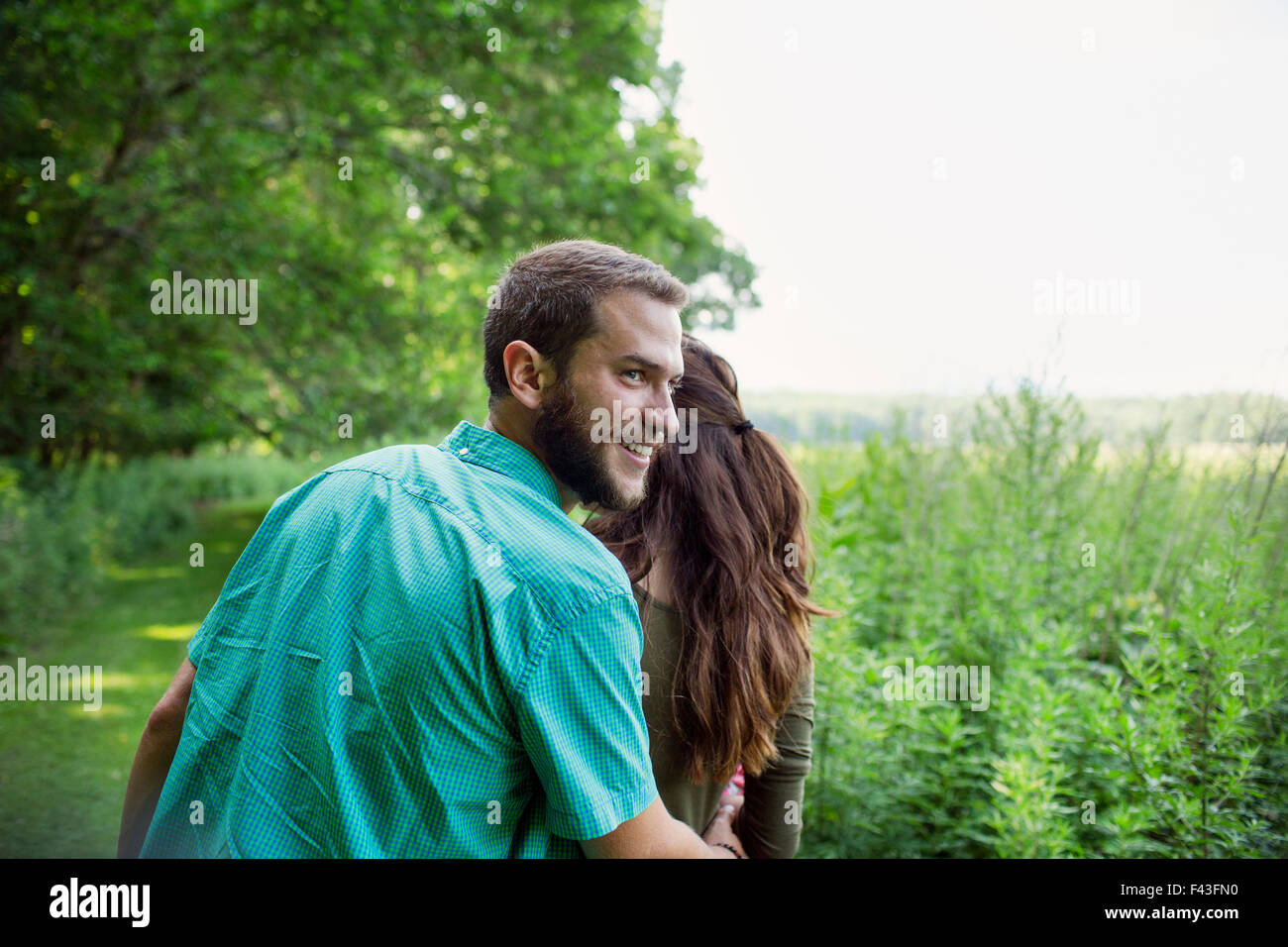 A man and woman walking through a meadow, through the long grass on a summer day. Stock Photo