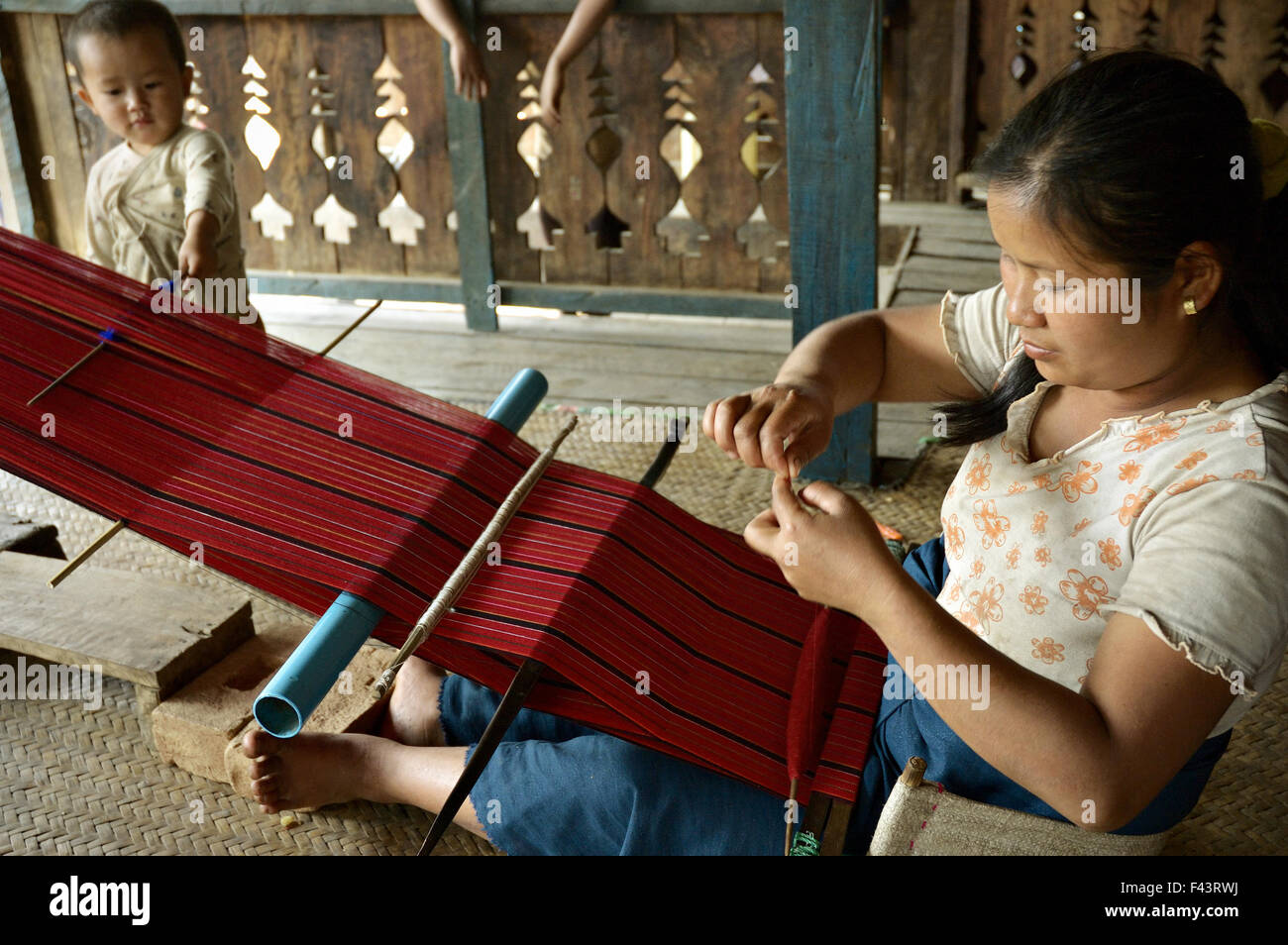 Palaung woman with her kid weaving with a loom inside her house in a village around Kengtung (Kyaingtong), Shan State, Myanmar Stock Photo