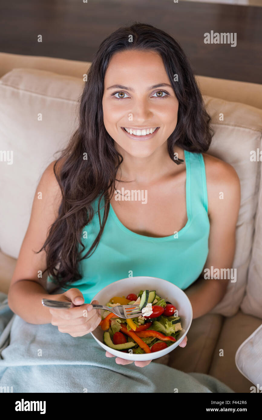 Pretty brunette eating salad on couch Stock Photo