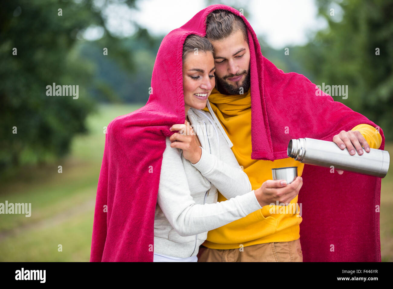 Happy couple under a blanket pouring hot drink Stock Photo