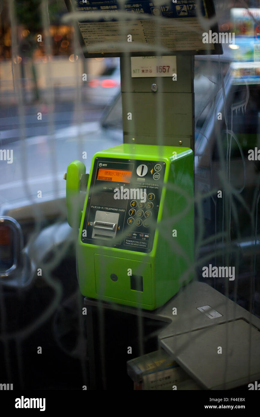 Public pay phone booth with green phone behind vandalized glass Stock Photo