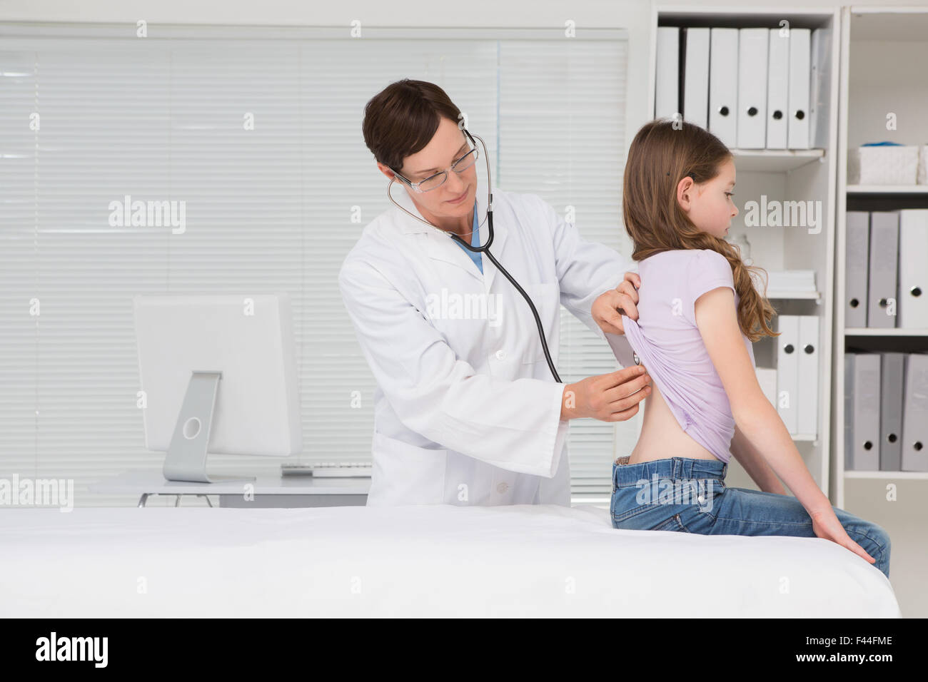 Doctor examining back of 8 year-old girl - Stock Image - C040/1357 -  Science Photo Library