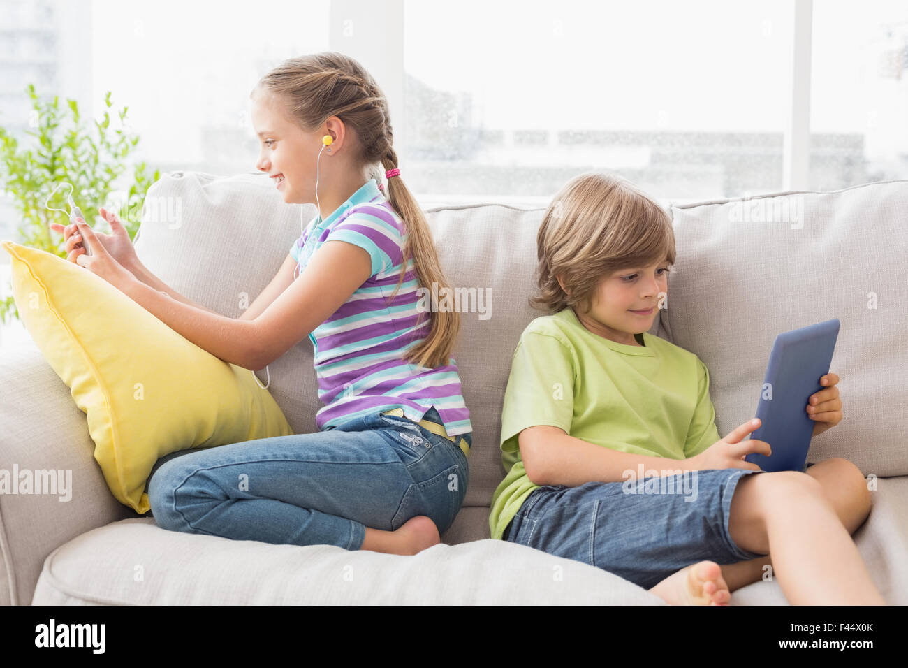 Siblings using technologies on sofa Stock Photo