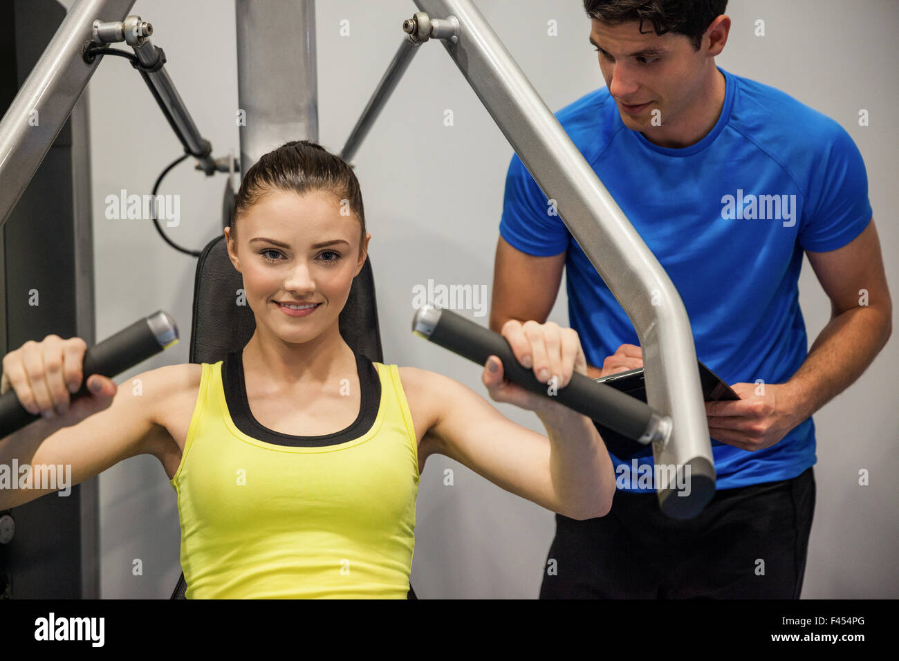 Confident woman using weights machine with trainer Stock Photo - Alamy