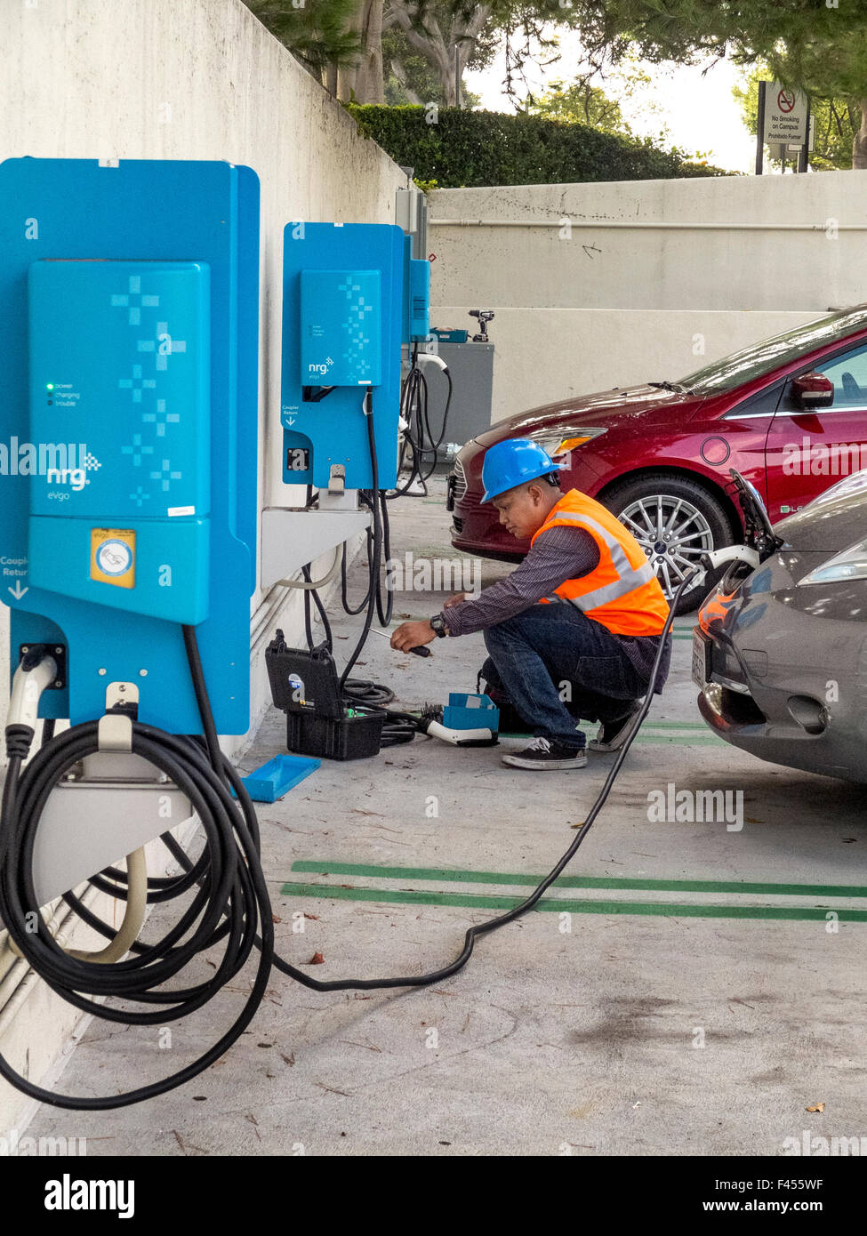 Repair technician maintains an electric car charging station at an Irvine, CA, hospital parking lot. Note electric car being charged at right. Stock Photo