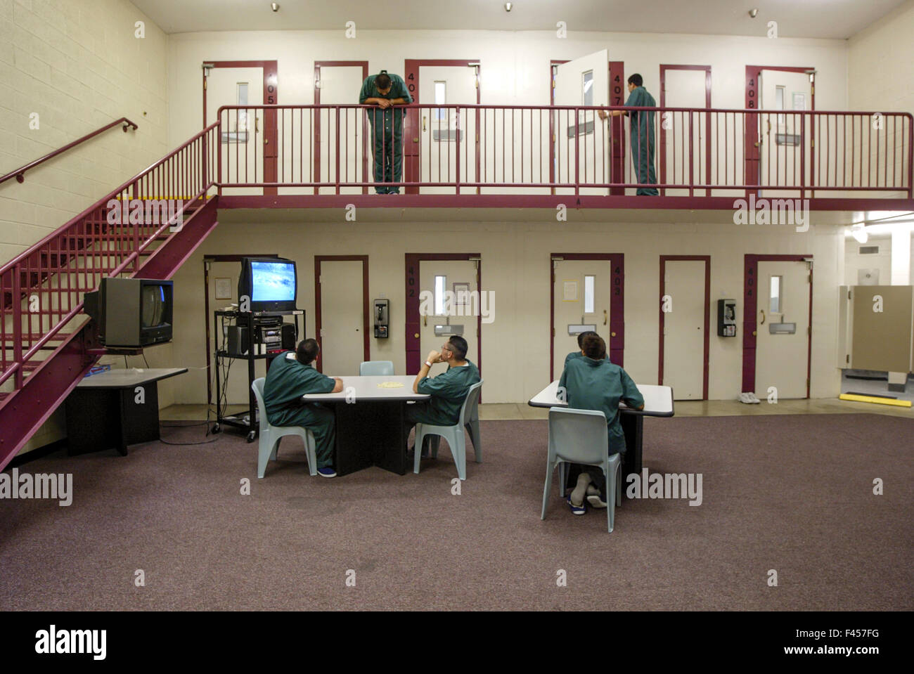 Uniformed multiracial teenage inmates of an Orange, CA, juvenile prison pass time in their day room watching television. Note cells at top. Stock Photo