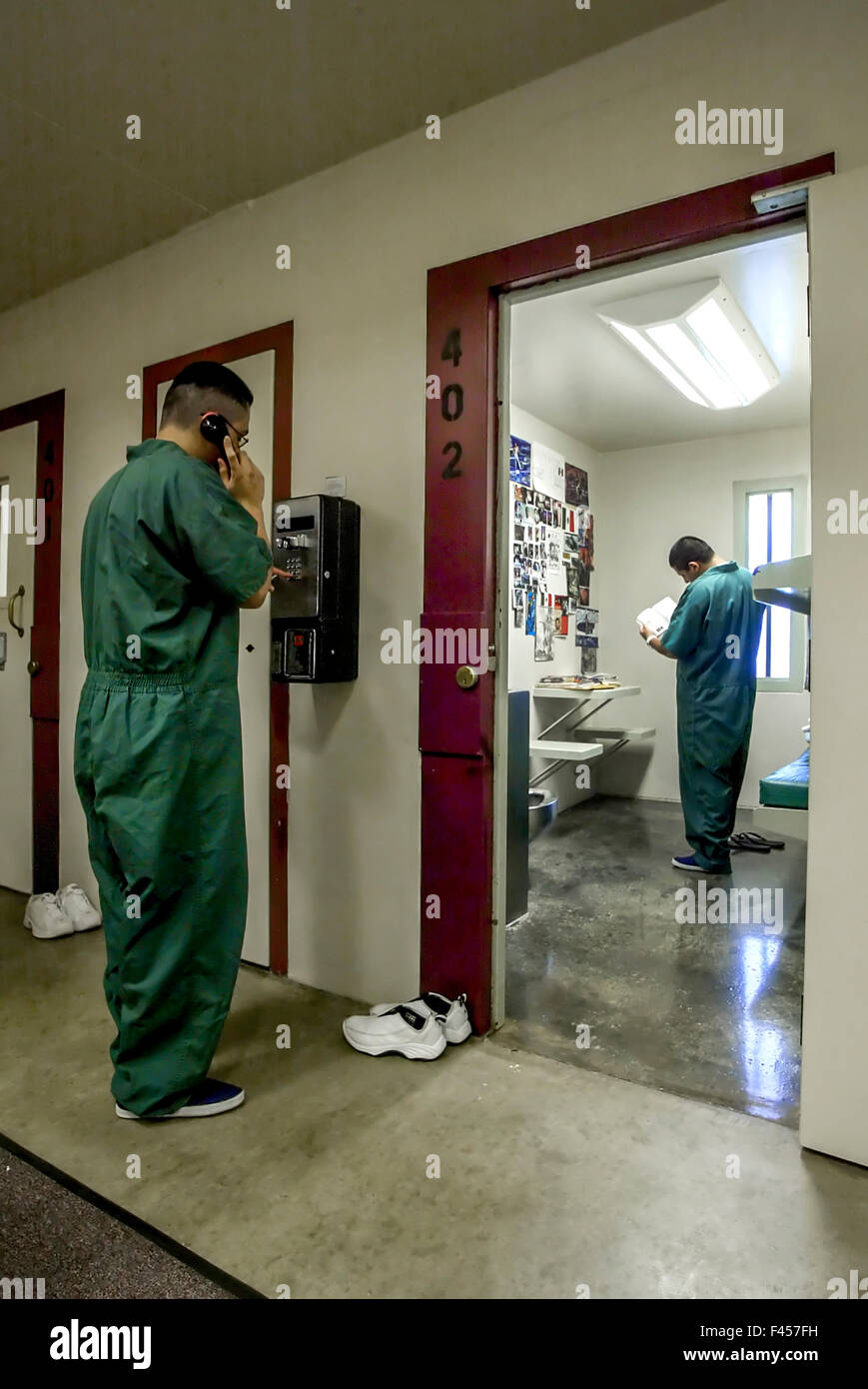 Uniformed Hispanic teenage inmates of an Orange, CA, juvenile prison use a pay telephone and read in their cell. Note lack of bars. Stock Photo