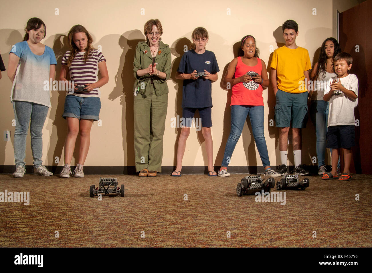 Excited multiracial preteens and a librarian watch a 'Robot Challenge Night' race at a public library multipurpose room in Laguna Niguel, CA. The remote control robots are assembled from a selection of snap-on spare parts. Stock Photo