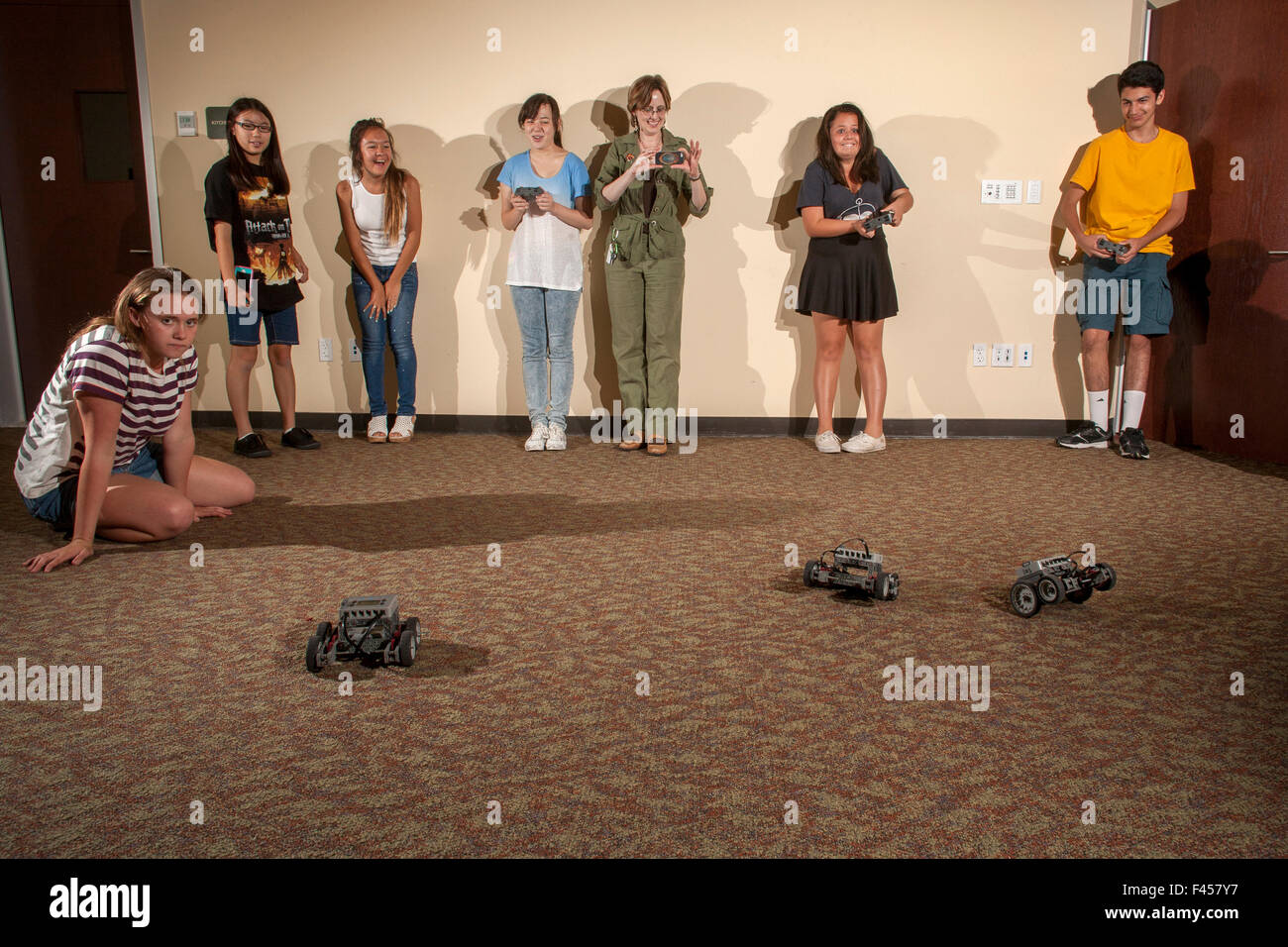 Excited multiracial preteens and a librarian watch a "Robot Challenge Night" race at a public library multipurpose room in Laguna Niguel, CA. The remote control robots are assembled from a selection of snap-on spare parts. Stock Photo