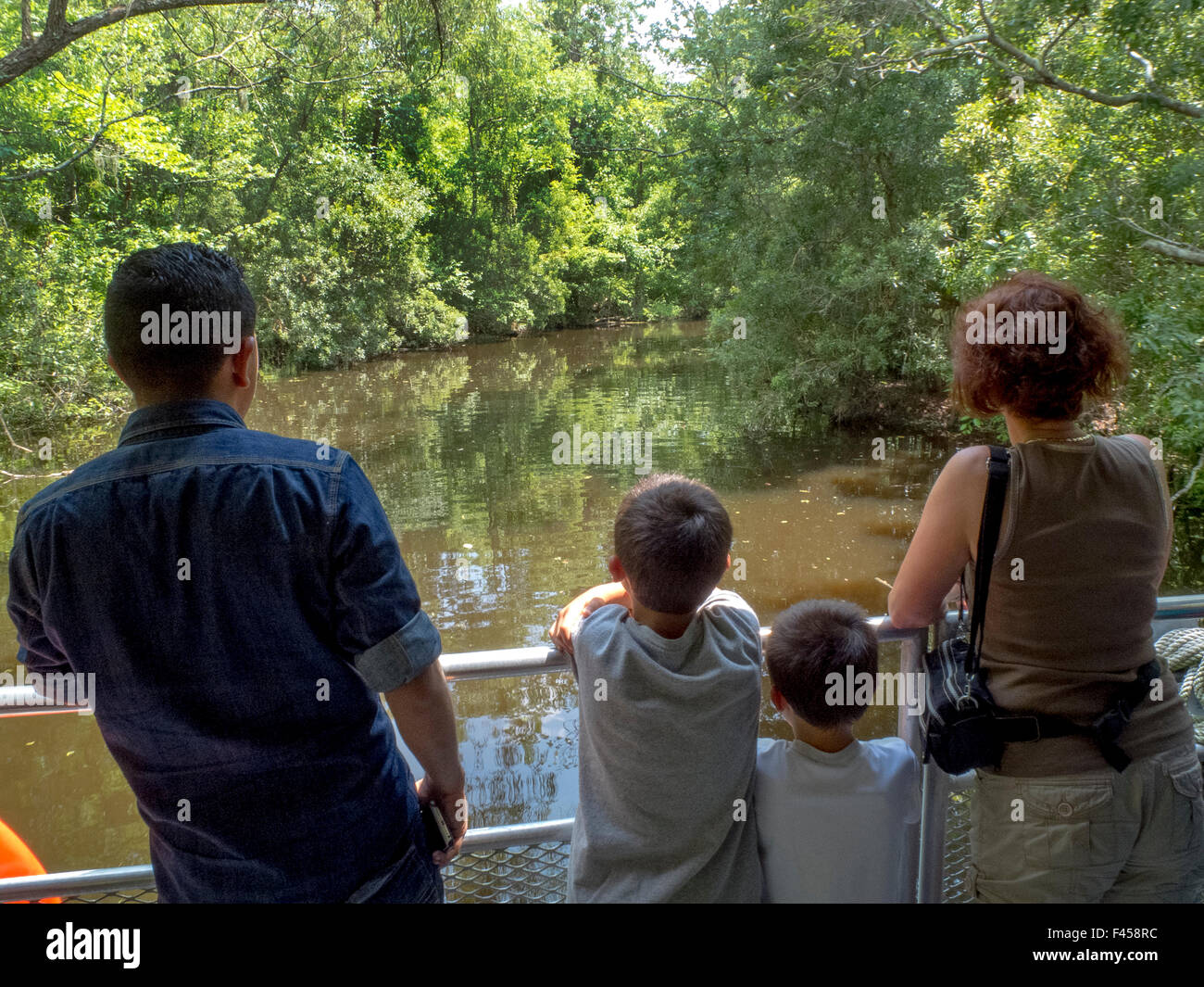 A tree-lined Mississippi River swamp bayou in Jean Lafitte National Park, Louisiana, is seen from the bow of a tour boat with tourists in the foreground. Stock Photo