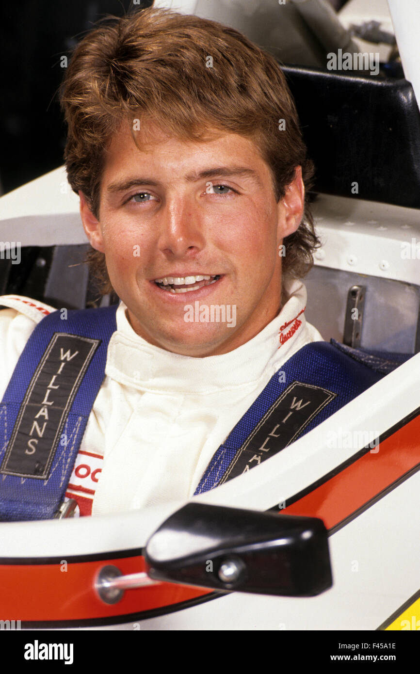 A handsome young race car driver poses in the cockpit of his car. Note seat belt and safety clothing. Stock Photo