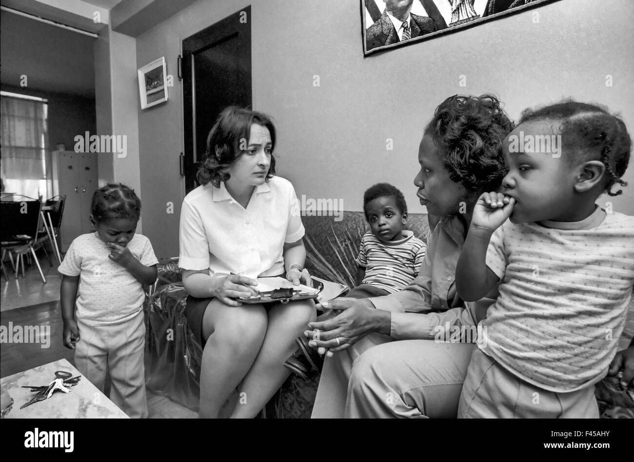 A Hispanic Boston social worker interviews an African American mother and her children in an inner city slum apartment about their eligibility for welfare. Note clipboard. Stock Photo