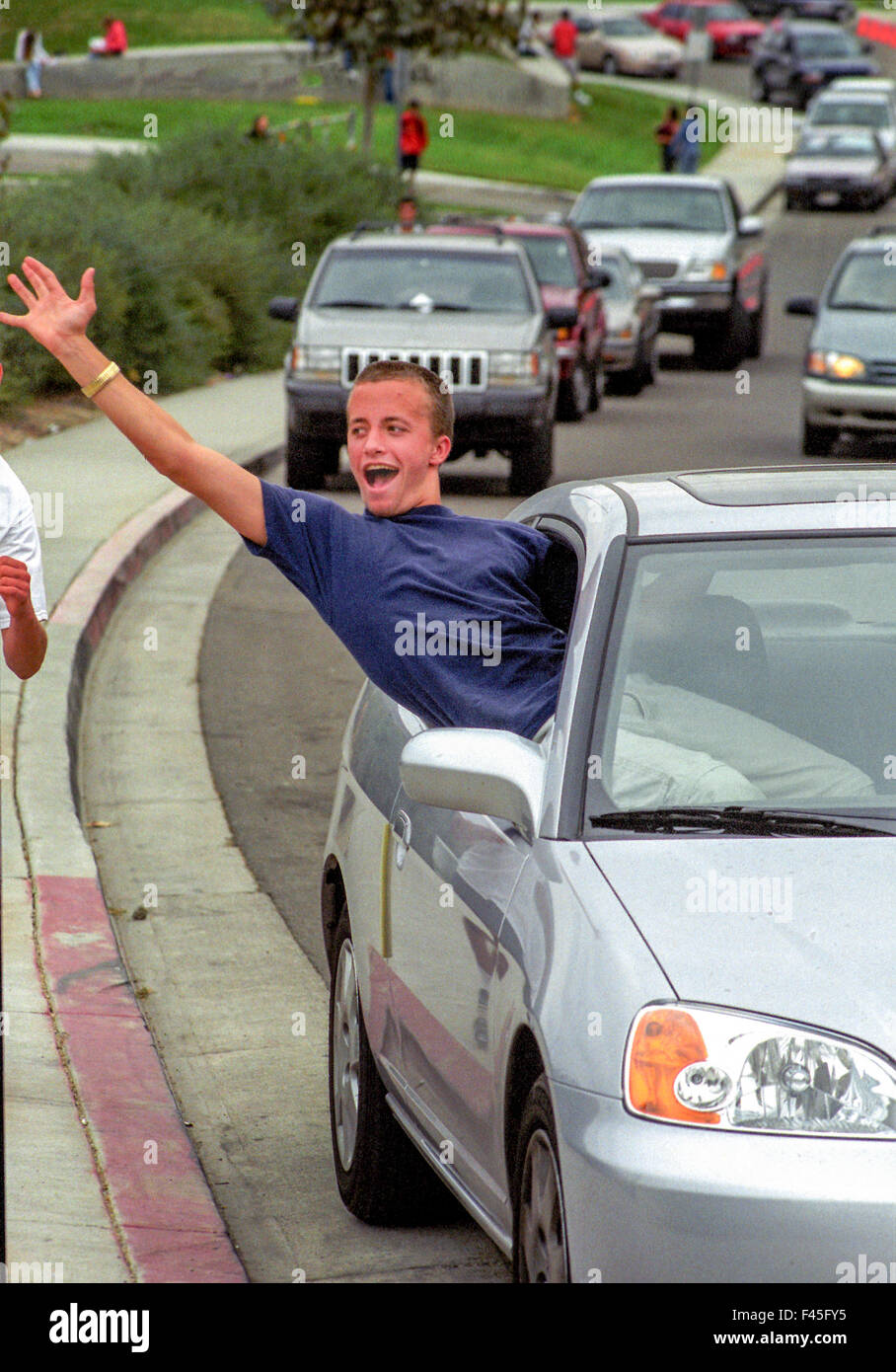 Leaving his seat belt unbuckled, a teen boy yells out of a car window