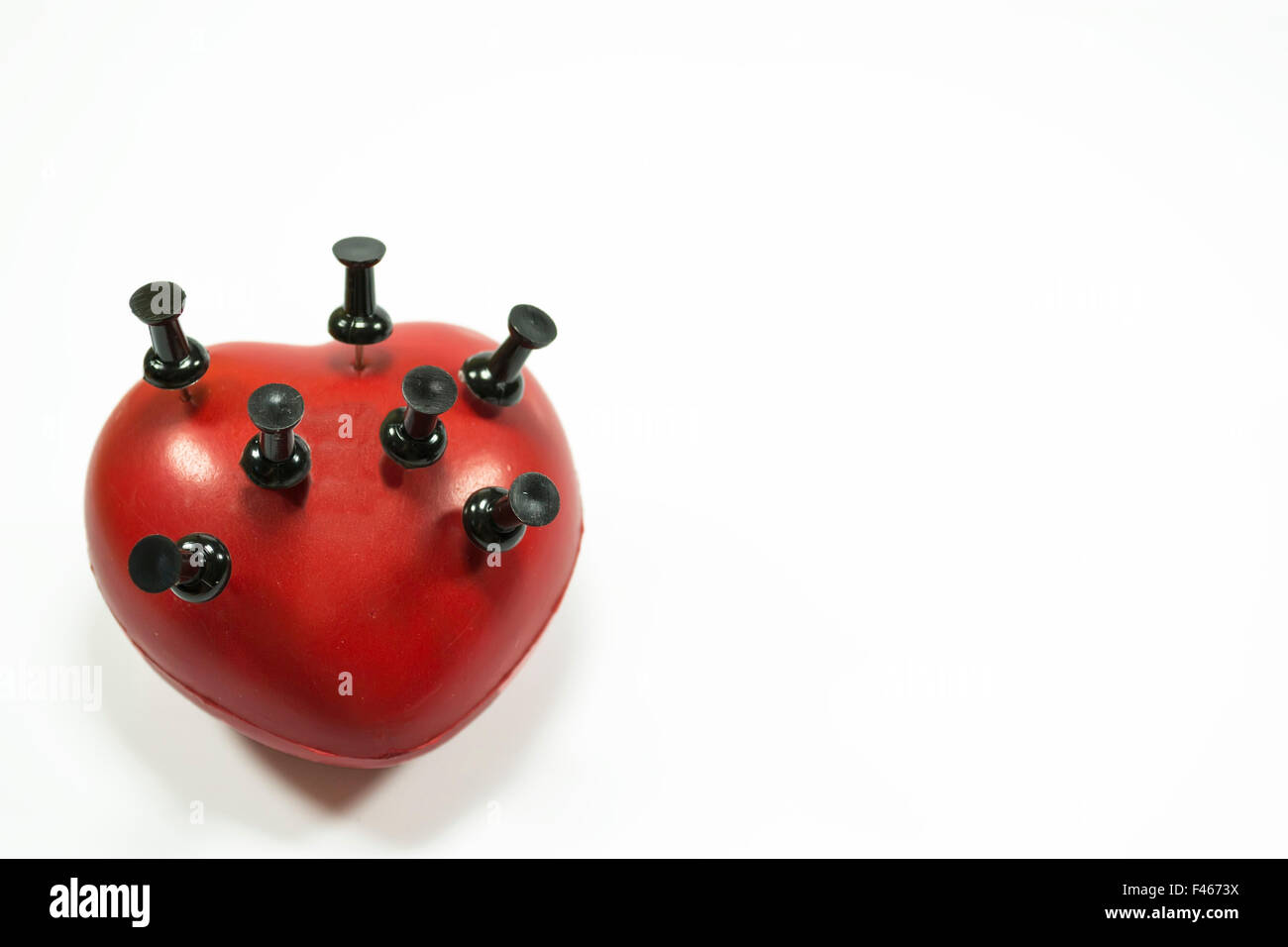 Red heart shape with black push pins puncturing it , conceptual image about heart related medical illnesses Stock Photo