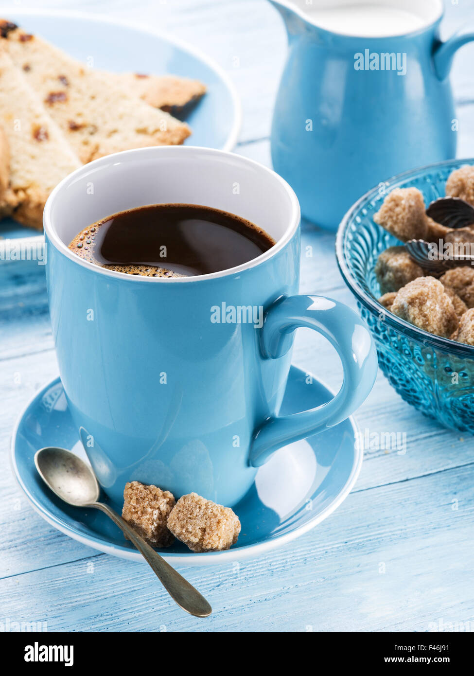 Cup of coffee, milk jug, cane sugar cubes and fruit-cake on old blue wooden table. Stock Photo
