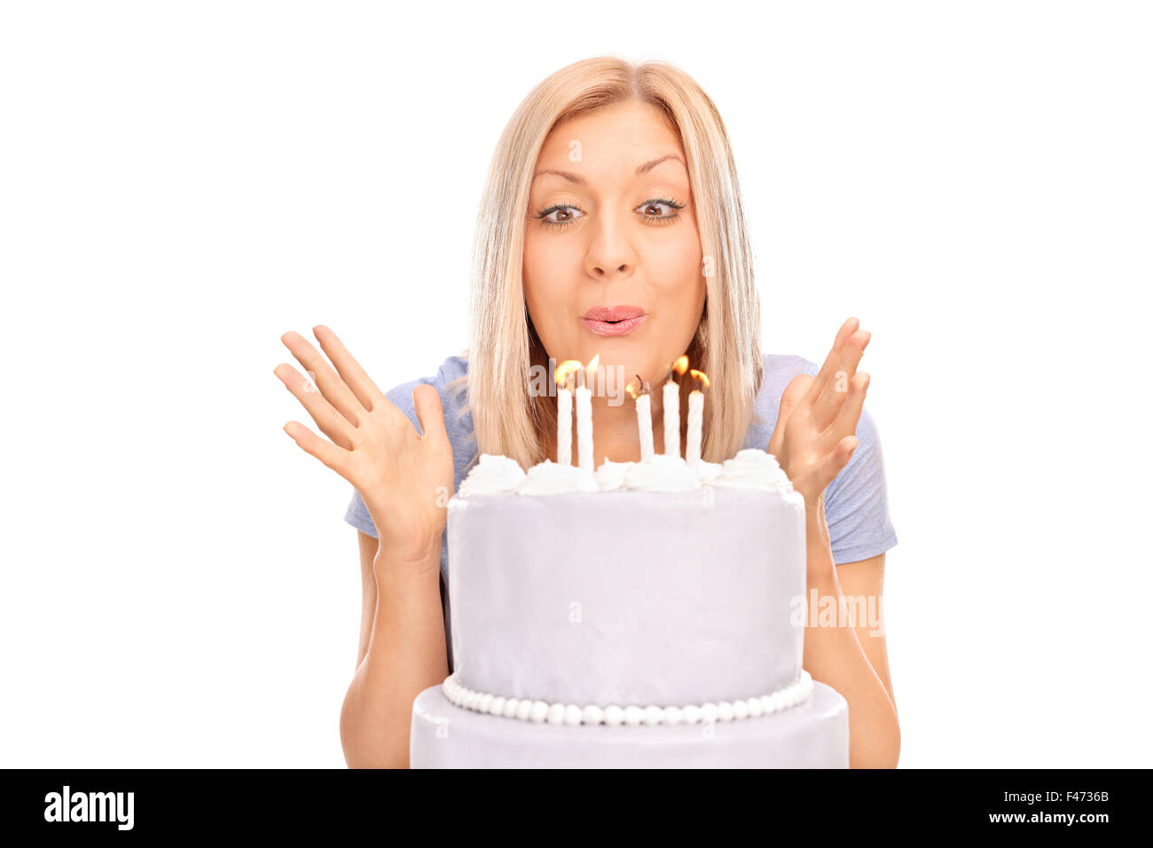 Studio shot of an overjoyed blond woman blowing candles on a birthday cake isolated on white background Stock Photo