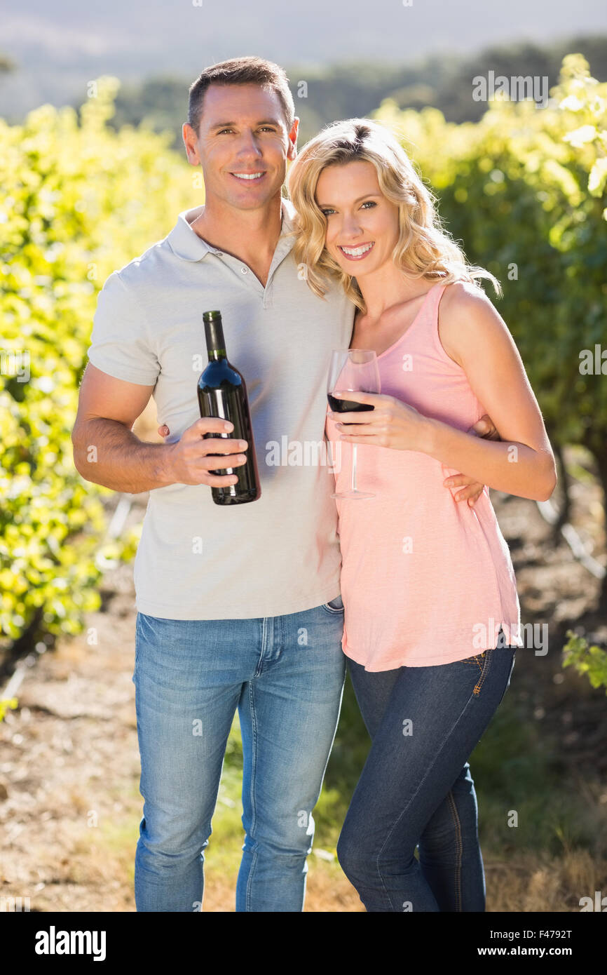 Smiling couple holding wine and standing in front of grapevine Stock Photo