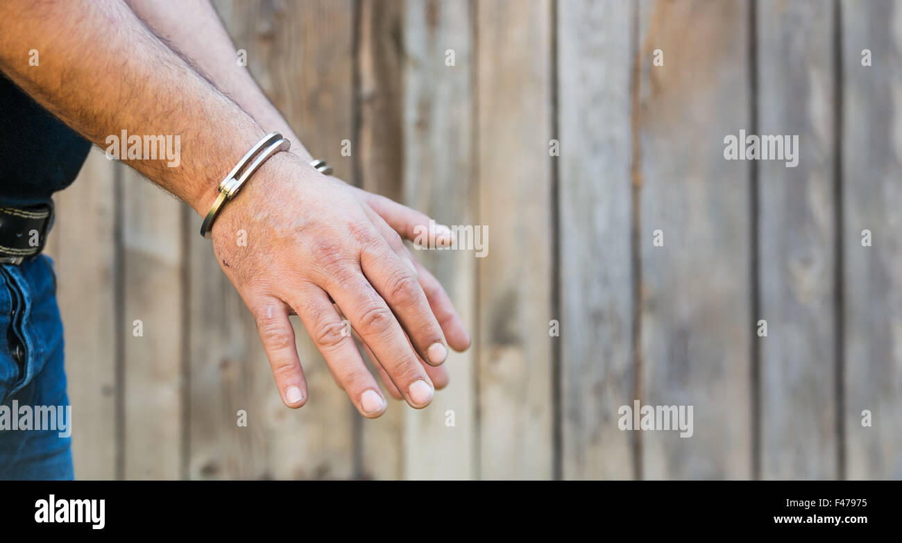 Arrest, closeup shot man's hands with handcuffs in front of plank wood