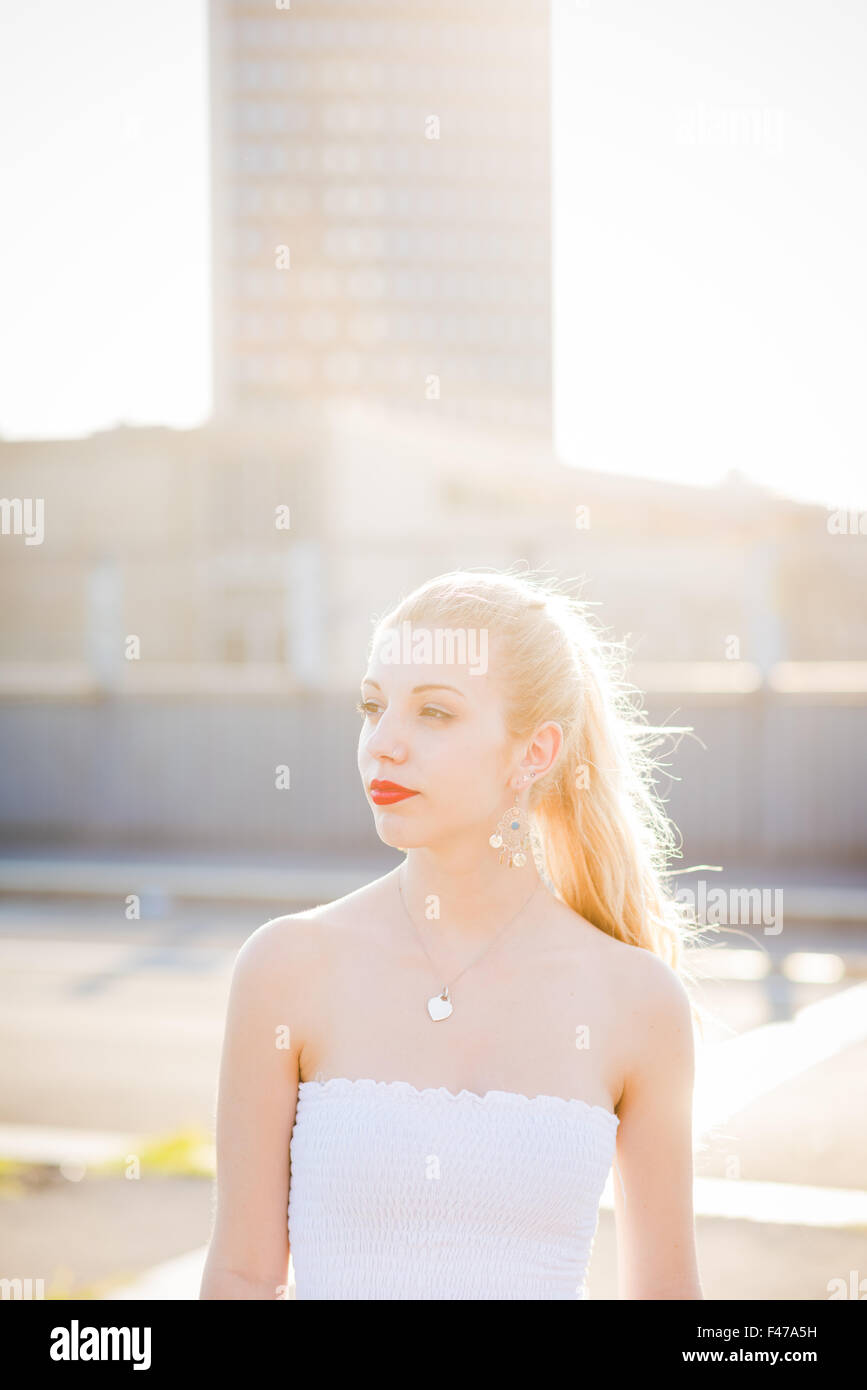 Half length portrait of young handsome caucasian long blonde straight hair woman overlooking right, serene - carefreeness, youth, thinking future concept - backlight Stock Photo