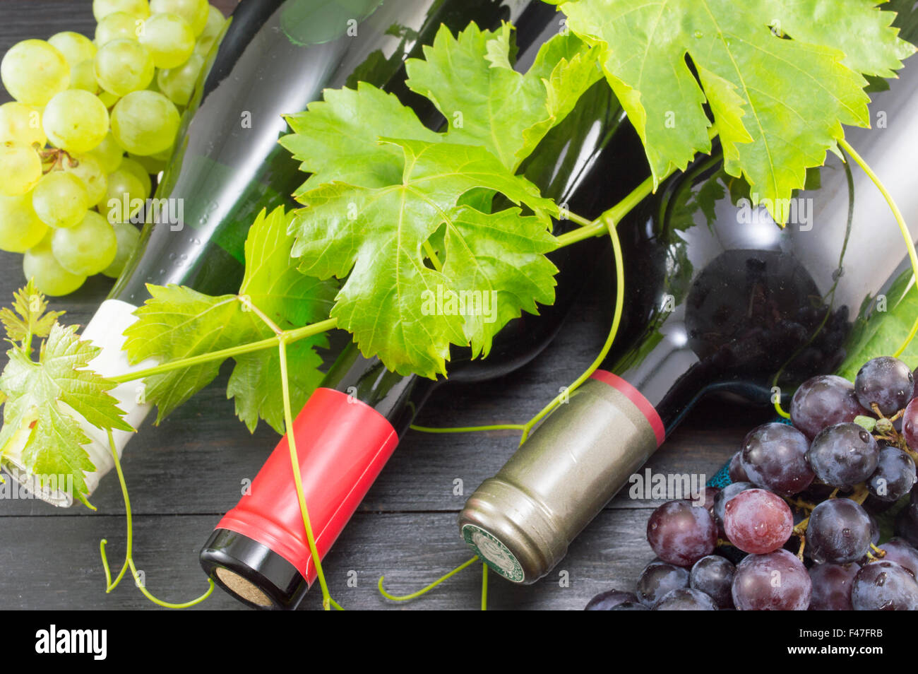 Three bottles of wine and grapes on dark wooden table Stock Photo