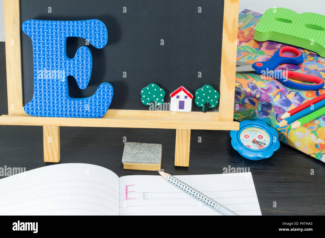 Learning the letter E. Blackboard, notebook, pencil and learning accessories Stock Photo
