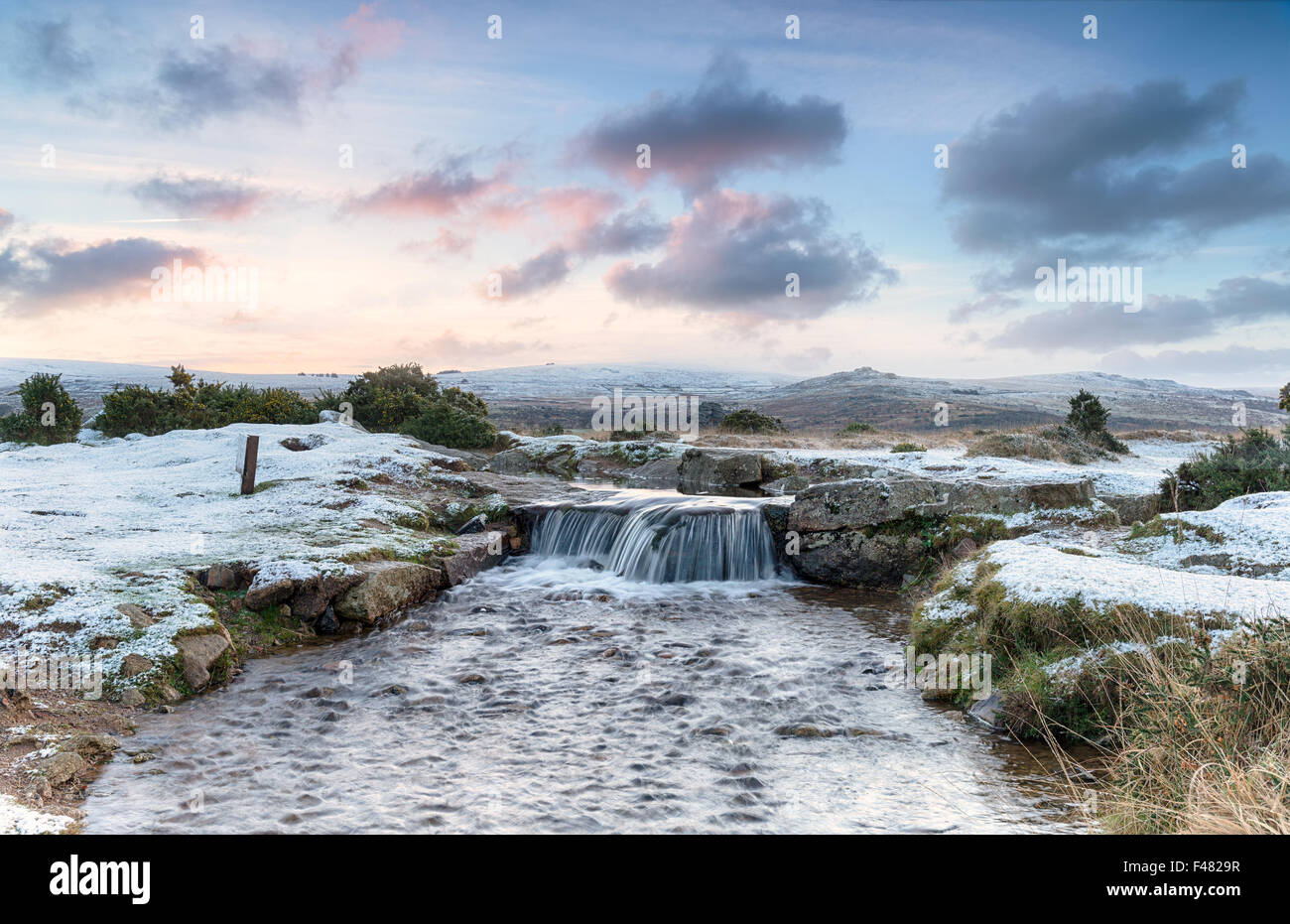 An idyllic winter scene with snow on the ground and a beautiful waterfall, on Dartmoor National Park in Devon Stock Photo