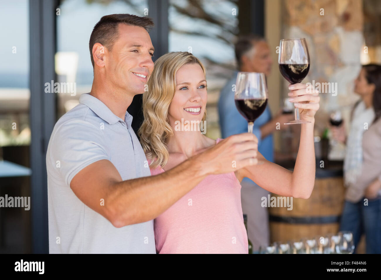 Smiling couple doing wine tasting and standing in front of couple drinking wine Stock Photo
