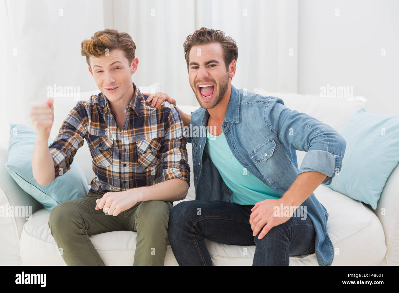 Happy homosexual couple cheering on sofa Stock Photo