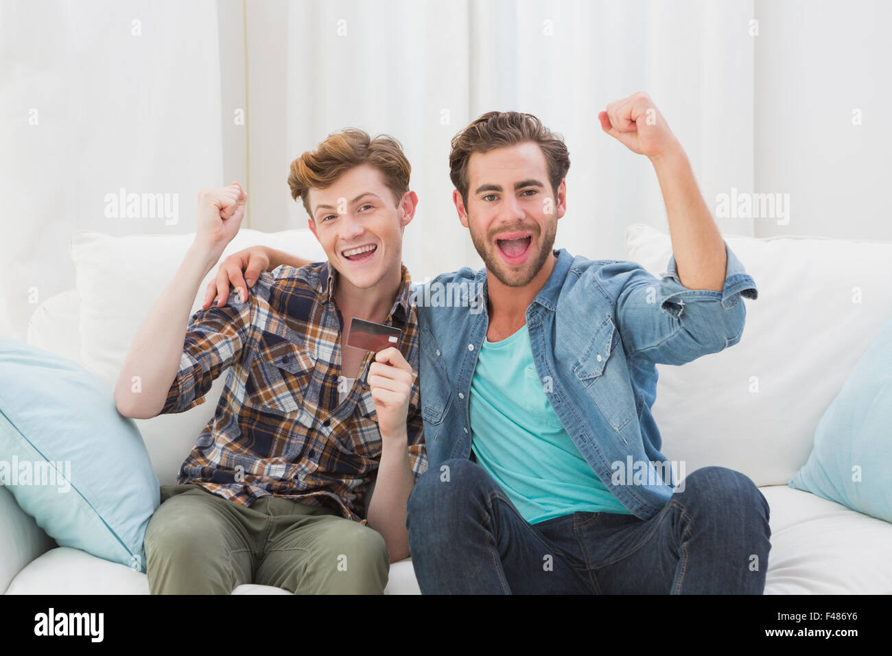 Happy homosexual couple cheering on sofa Stock Photo