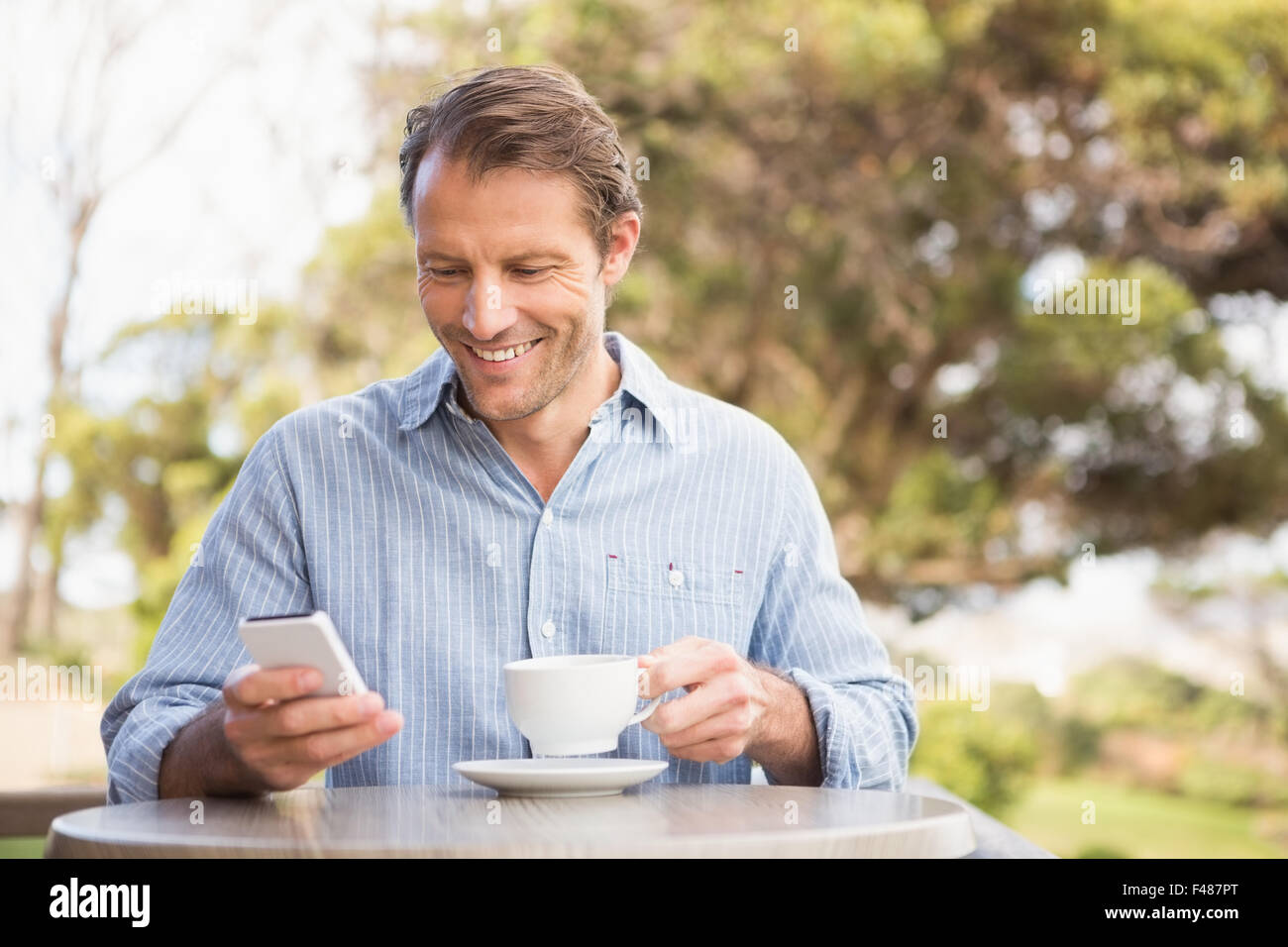 Smiling farmer using a smartphone while drinking a coffee Stock Photo