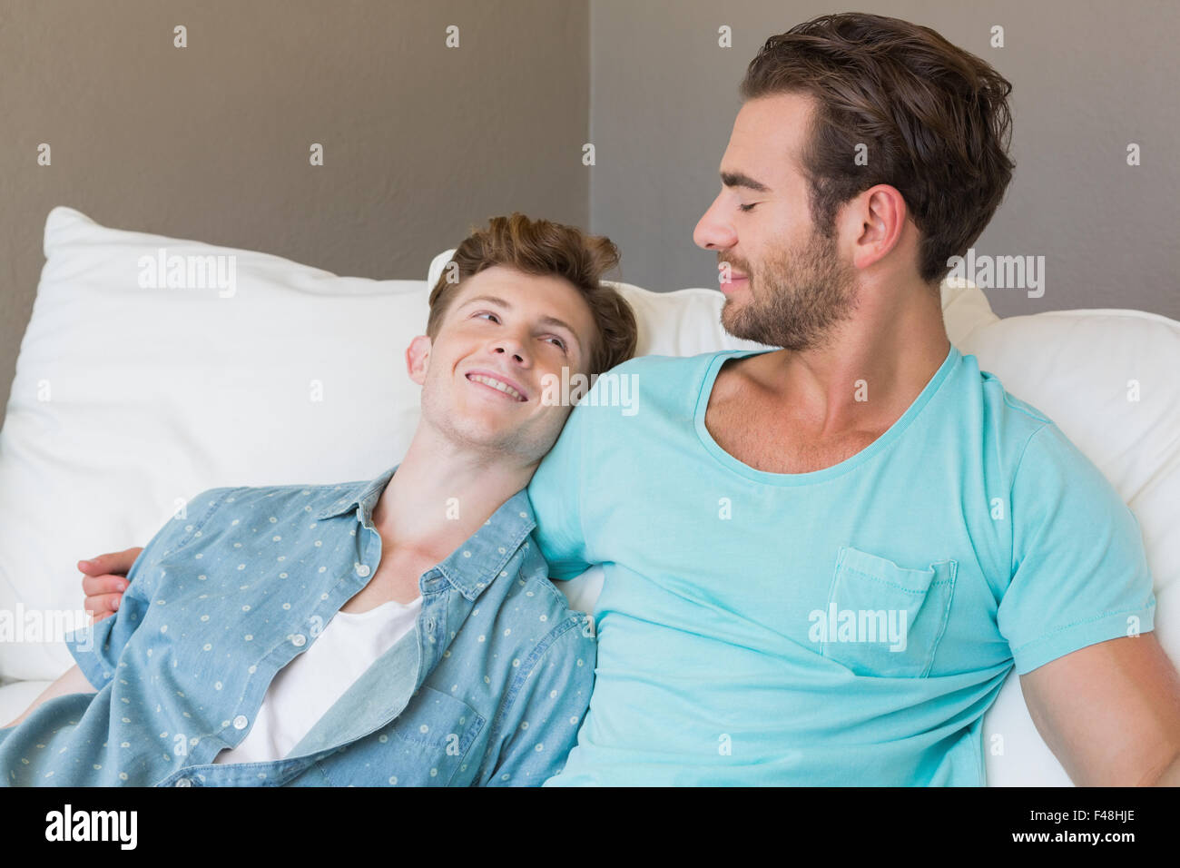 Happy homosexual couple hugging and looking at each other on couch Stock Photo