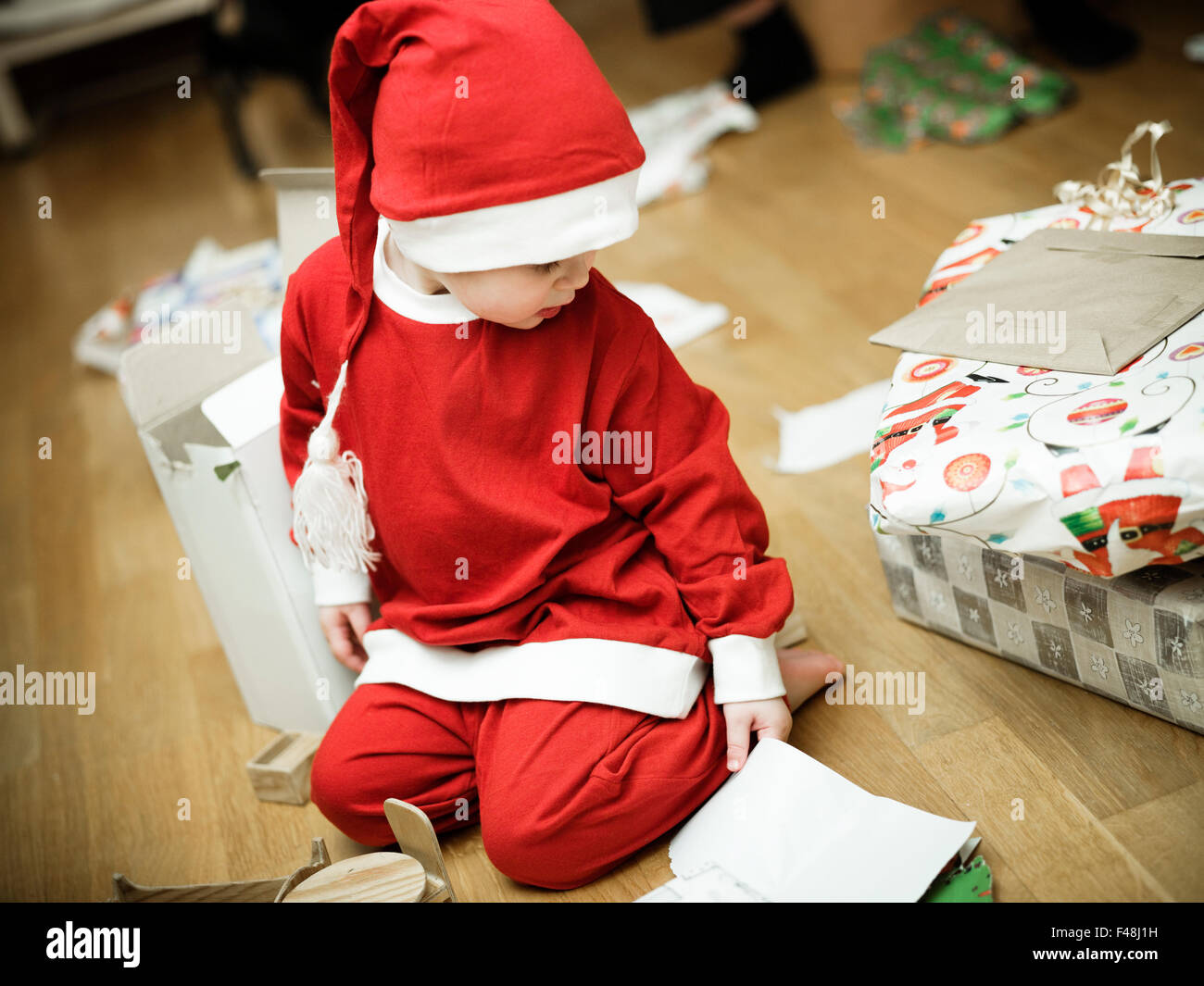 Girl dressed as Santa Claus opening Christmas presents, Sweden. Stock Photo