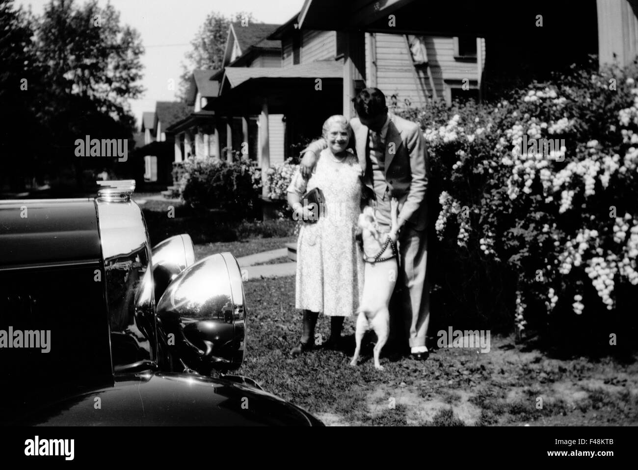 Old woman, dog, and young man in neighborhood housing with 1930s car Stock Photo