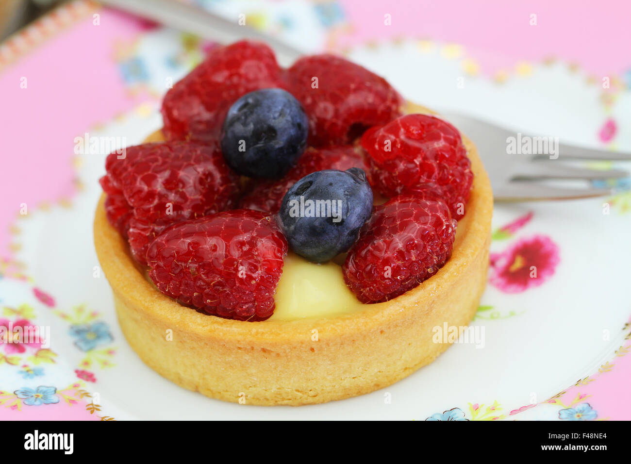 Delicious crunchy tartelette with custard, fresh raspberries and blueberries, closeup Stock Photo