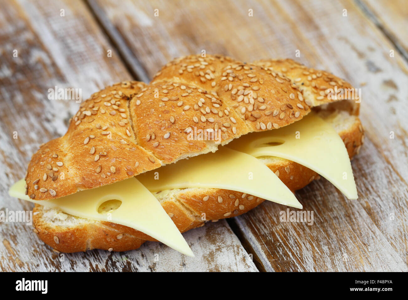 Crunchy sesame seeds bread roll with Swiss cheese on rustic wooden